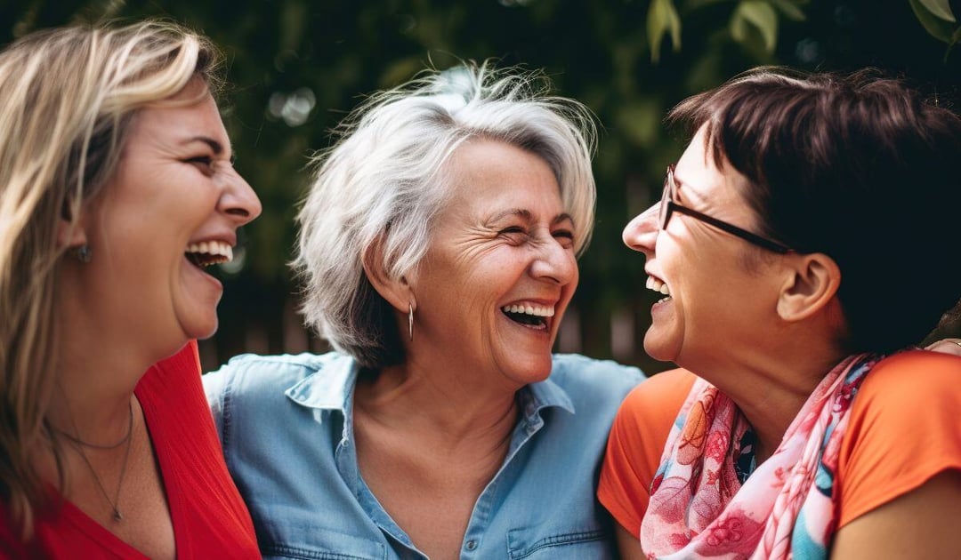 Three older women laughing and chatting outdoors