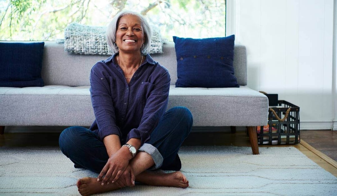 Older African American women sitting on the floor in her living room practicing yoga