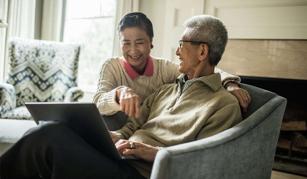 Older Asian couple looking at laptop while seated on a sofa