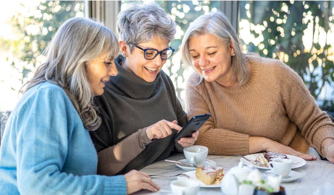 Three older woman in a cafe looking at a smartphone