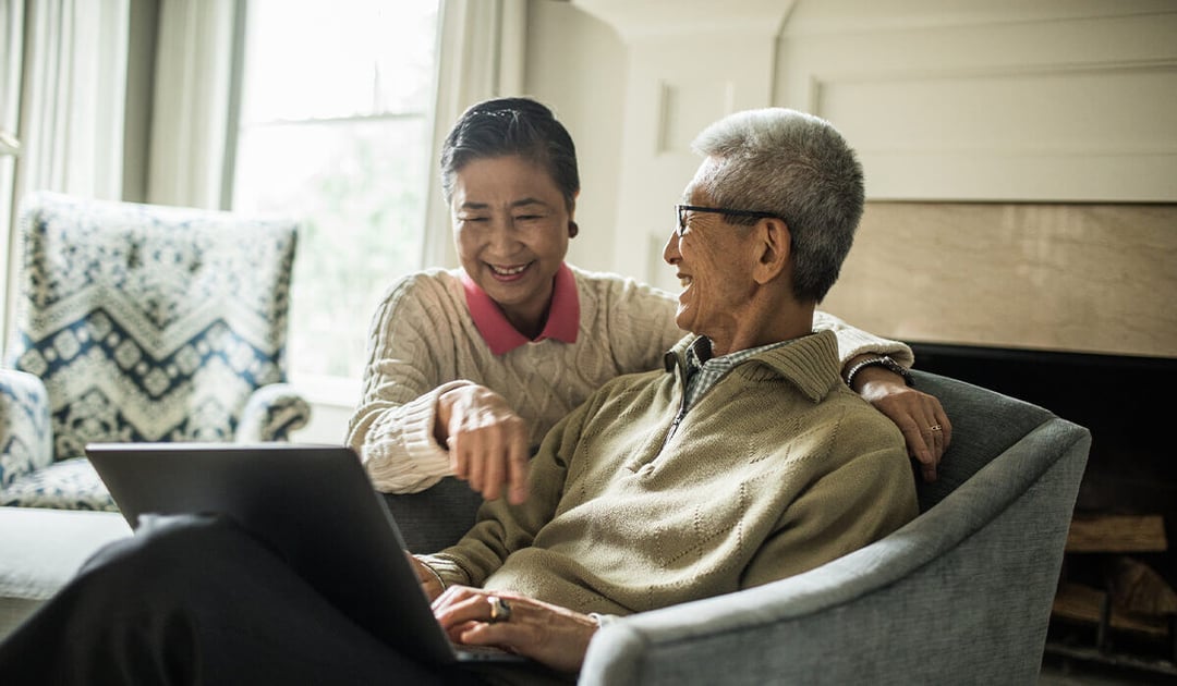 Older Asian couple looking at a laptop computer while sitting on a sofa